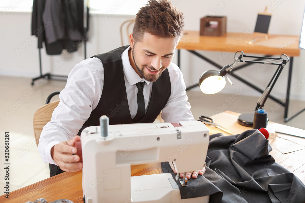 Young male tailor working on sewing machine in atelier