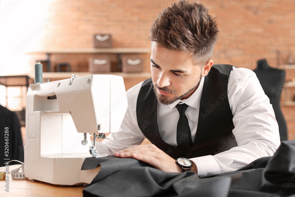 Young male tailor working on sewing machine in atelier