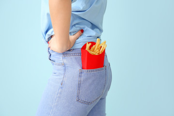 Young woman with french fries in pocket on color background, closeup