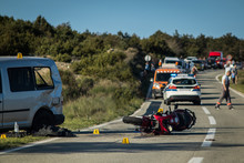 Car And A Red Sport Motorcycle Crash Scene On An Open Road In Afternoon. Workers And Police Seen Around The Crash Site, With A Queue Of Traffic Building Behind. Destroyed Van And Motorcycle.