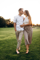 Wall Mural - Happy couple in love in casual wear walks barefoot on the grass at sunset and hugging