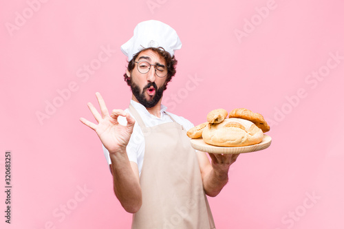 Fotomural young crazy baker man holding bread against pink wall