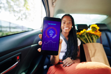 Happy young woman checking weather forecast via smartphone application when riding in taxi