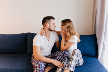 Young people in cute pajama looking at each other. Lovely blonde girl in checkered pants embracing her boyfriend.