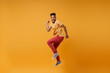 Joyful young african american guy in casual clothes posing isolated on yellow orange wall background studio portrait. People lifestyle concept. Mock up copy space. Jumping clenching fists like winner.