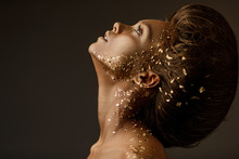 Fashion Art Portrait Of Model Girl With Holiday Golden Shiny Professional Makeup. Beaty Woman With Gold Metallic Body And Hair On Dark Background. Gold Glowing Skin. Copy Space