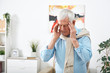 © pressmaster - Tired senior man in blue shirt touching his temples while feeling headache after working at home
