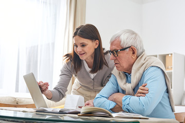 Poster - Young brunette woman pointing at laptop display while showing her senior father how to make online shopping