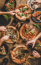 Friends Having Pizza Party Dinner. Flat-lay Of People Eating Different Kinds Of Italian Pizza, Salad And Drinking Red Wine Over Wooden Table, Top View. Fast Food Lunch, Gathering, Celebration
