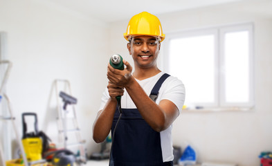 Poster - profession, construction and building - happy smiling indian worker or builder in helmet with electric drill or perforator over home or apartment room background