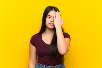 Wall Mural - Young teenager Asian girl over isolated yellow background covering a eye by hand