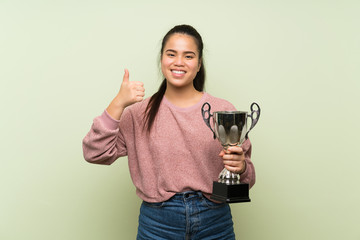 Wall Mural - Young teenager Asian girl over isolated green background holding a trophy