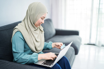 Wall Mural - Female muslim woman using laptop while holding credit card.