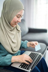 Wall Mural - Female muslim woman using laptop while holding credit card.