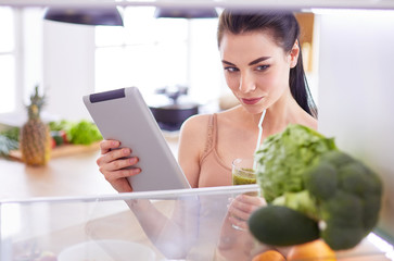 Young woman with glass of tasty healthy smoothie at table in kitchen