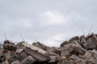 A pile of large gray concrete fragments with protruding fittings against a cloudy sky.