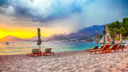 Wall Mural - Dramatic sunset at beach with chaise lounges and umbrellas in Sveti Stefan near Budva