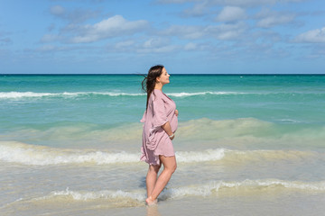 Wall Mural - Pregnant caucasian brunette woman  stands on the shore of the Atlantic ocean at midday, Cuba