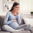 © Prostock-studio - Pregnant Lady Coughing Feeling Sick Touching Mouth Sitting On Sofa