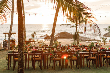 wooden tables for wedding dinner decorated with tropical flowers, pineapples, coconuts and glass lam