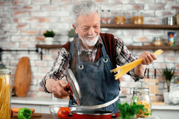 Wall Mural - Man in kitchen. Old man cooking pasta. 