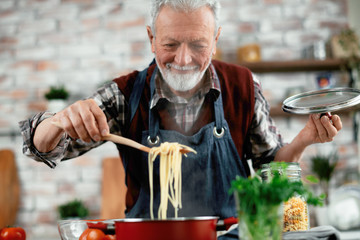 Wall Mural - Man in kitchen. Old man cooking pasta. 