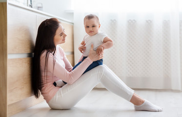 Wall Mural - Happy mother playing with her cute baby son on kitchen floor