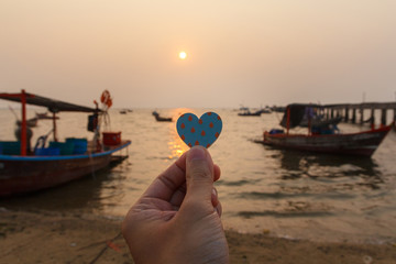 Close up of hand man holding a paper heart with the sea background in evening. love concept, happy valentine.