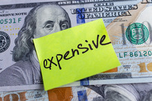 Yellow Stick Note On An USD Money Background. The Inscription "expensive" On A Yellow Memory Sticky Note