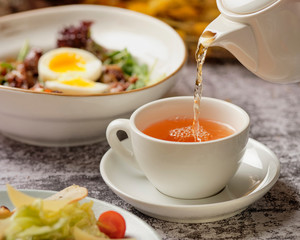 Tea being poured into tea cup. Cafe or bar table with dinner and tea. Communication concept. Restaurant background.