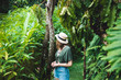 A young woman in a hat stands on the background of huge green tropical plants, Bali. A girl walks among the jungle. Girl and fairytale nature enjoying nature and fresh air.