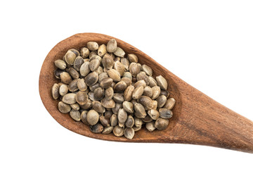 Wall Mural - Close up of brown wooden spoon with hemp seeds from lower right corner seen directly from above and isolated on white background