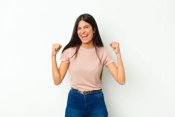 Wall Mural - young pretty latin woman feeling happy, positive and successful, celebrating victory, achievements or good luck against flat wall