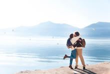 Young Couple In Love Hugging And Kissing At Winter Sea Beach. Travelers At Blue Background Of Mountains And Seagulls. Happy Man And Woman In Vacation, Adventure. Romantic Lifestyle Moment. Copy Space