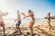 Group of happy and joyful young people having fun together in friendshp with a battle of waterguns at the beach during summer vacation - friends have fun at the beach in sunny day