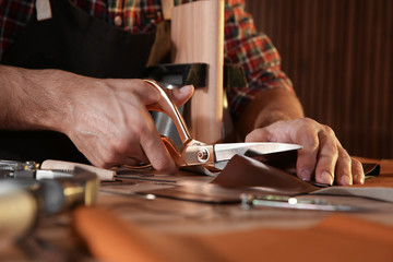 Wall Mural - Man cutting leather with scissors at table, closeup