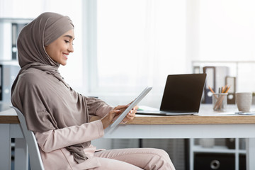 Wall Mural - Smiling Islamic Businesswoman Using Digital Tablet While Sitting At Workplace