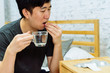 © twinsterphoto - Young Asian man feeling sick and taking pills while sitting on the bed at home with medicines tablets and drinking water on table. Healthcare and Medicine concept