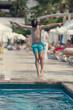 Caucasian boy having fun making high jump to plunge into swimming pool at resort.