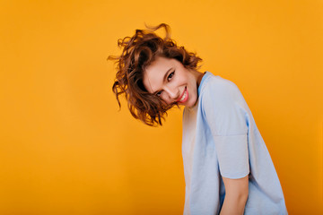 Funny inspired girl with brown hair playfully posing on yellow background. Studio portrait of cheerful white woman with trendy haircut.