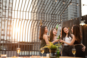 Group of young beautiful happy asian women holding bottle of beer chat together with friends while celebrating dance party on outdoor rooftop nightclub with copy space for advertising.