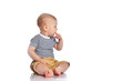 Thoughtful infant baby boy toddler is sitting on the floor with his finger at his mouth looking at copy space near him