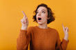 © Look! - Close-up portrait of enthusiastic girl with suprised face expression looking around. Studio shot of lovable curly lady isolated on orange background.