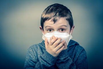 child with face mask wraps his hands over his mouth.