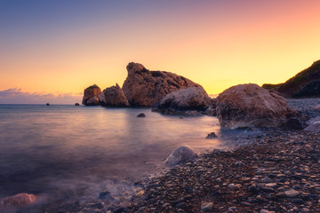 Wall Mural - Amazing sunset seascape, famous Love beach on Cyprus with rocks and sea pebbles, travel background. Aphrodite's Rock beach or Petra tou Romiou, the birthplace of Goddness Aphrodite, Paphos