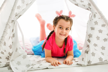 Wall Mural - A little girl sits in a wigwam with pillows