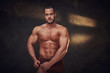 © Fxquadro - Pensive muscular bodybuilder is demonstrating his leg muscles at dark photo studio.