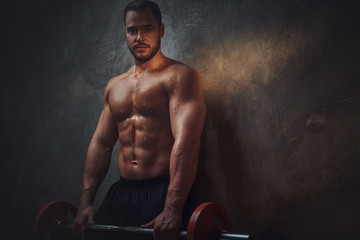 Wall Mural - Portrait of handsome man with barbell in hands in the dark photo studio.