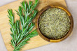 Top view of bright fresh green and dried rosemary branches, twigs and leaves in a wooden bowl and board on light background.