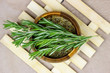 Top view of bright fresh green and dried rosemary branches, twigs and leaves in a wooden bowl and board on light background.